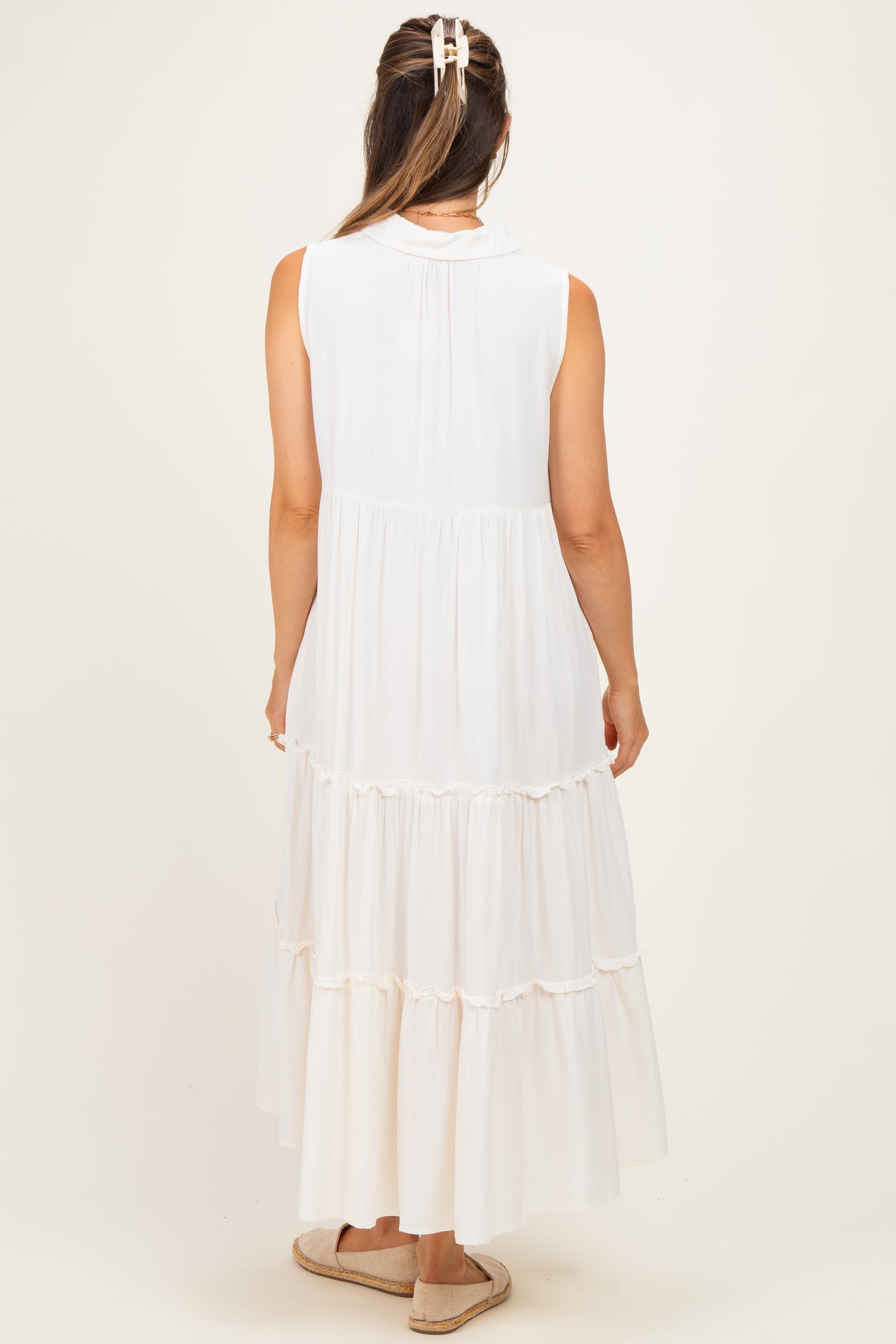 woman wearing a sleeveless white maternity maxi dress with tiered ruffles and a back pleat