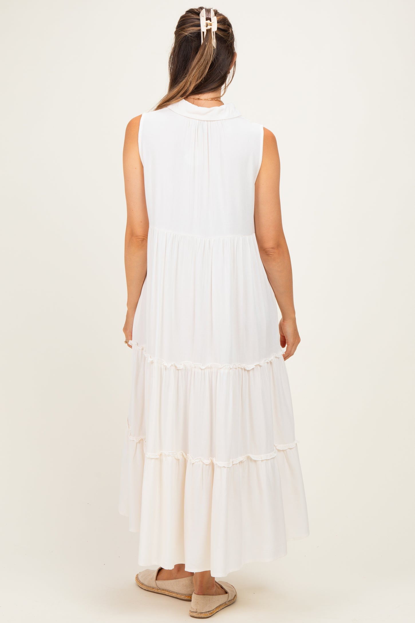woman wearing a sleeveless white maternity maxi dress with tiered ruffles and a back pleat