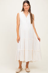 woman wearing a white sleeveless maternity dress with a button closure and tiered ruffle hem, showing her baby bump