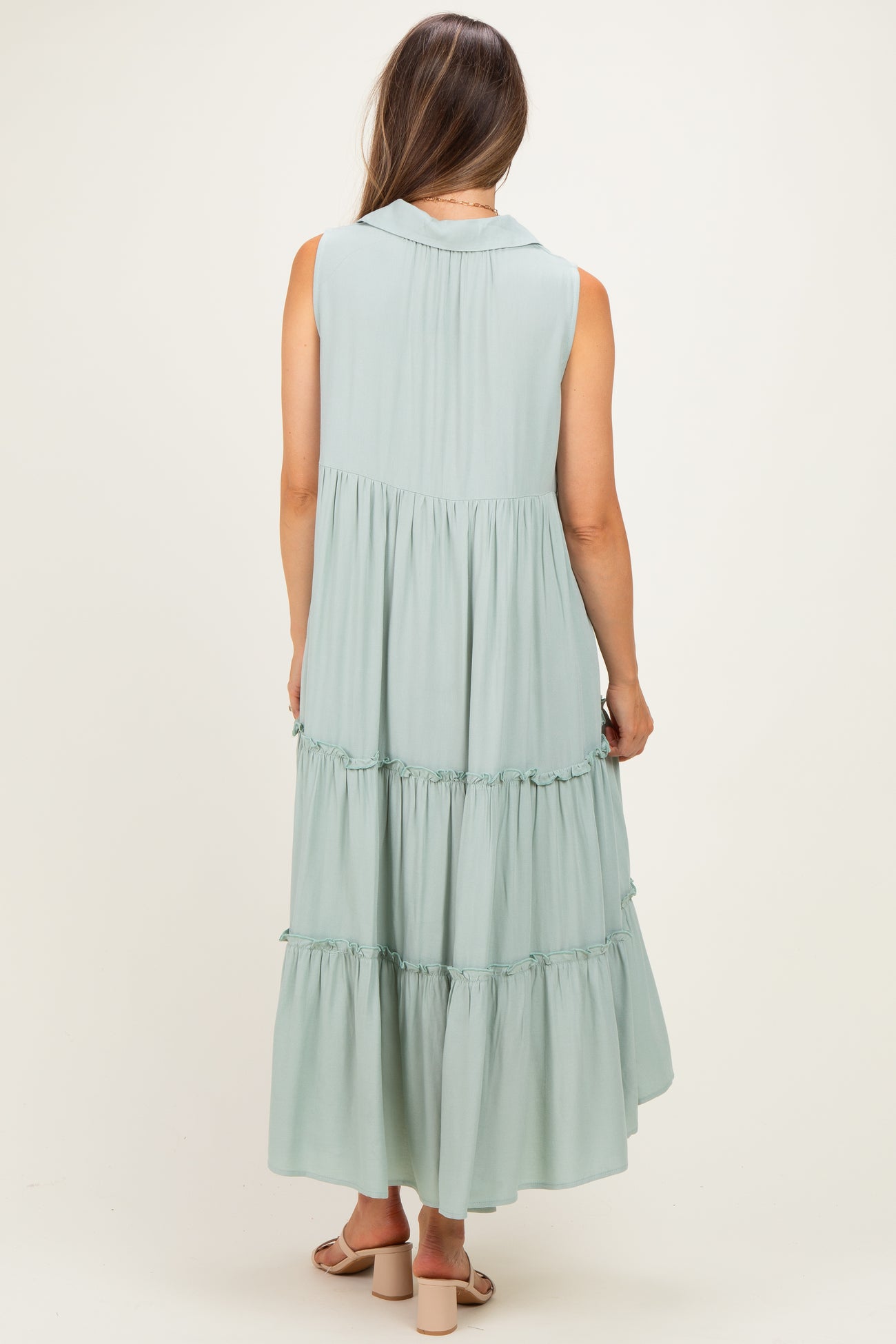 woman wearing a sleeveless light green maternity maxi dress with tiered ruffles, showing the back view