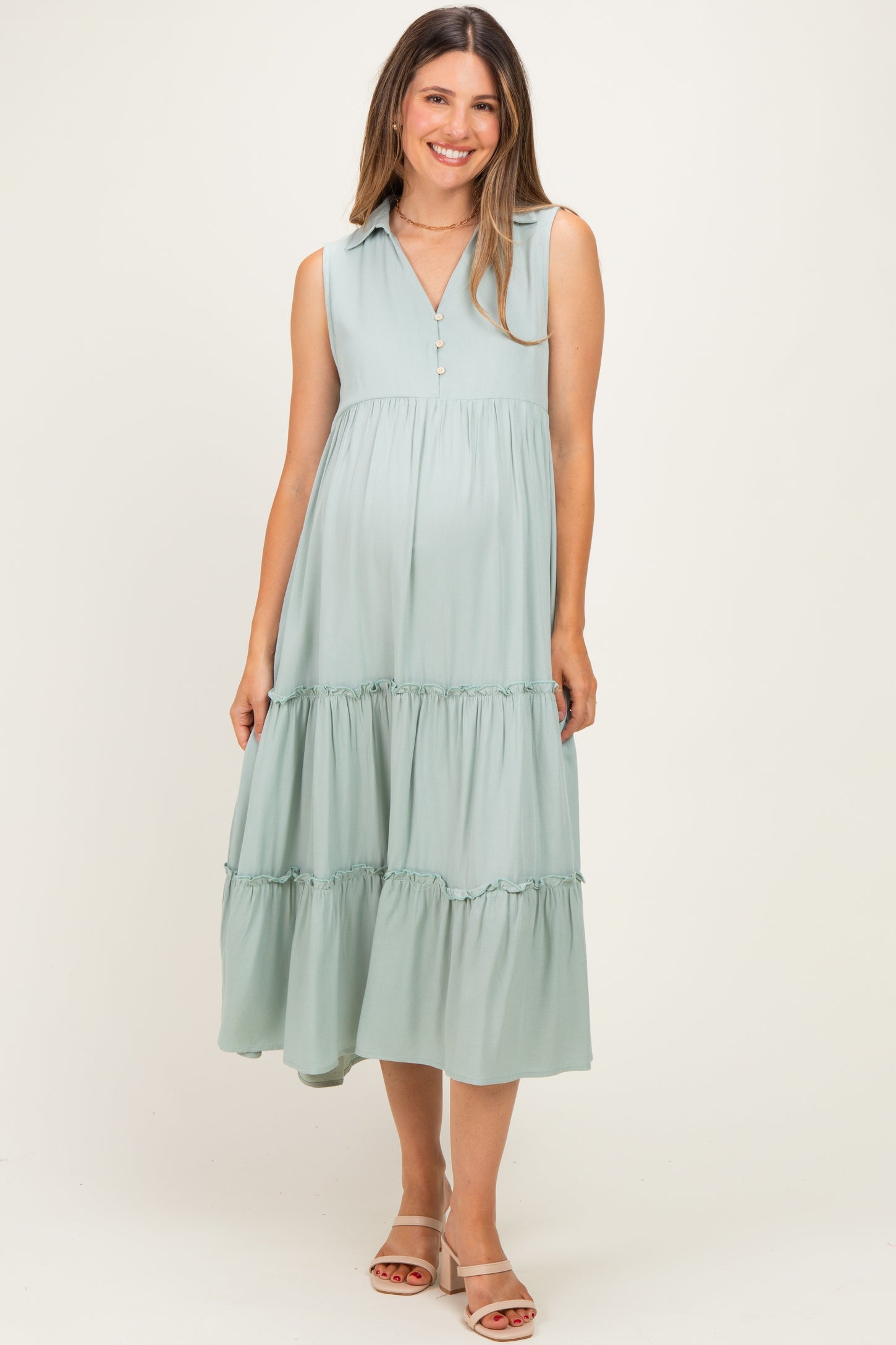 woman wearing a mint green sleeveless maternity dress with a v-neck and tiered skirt, showing a baby bump