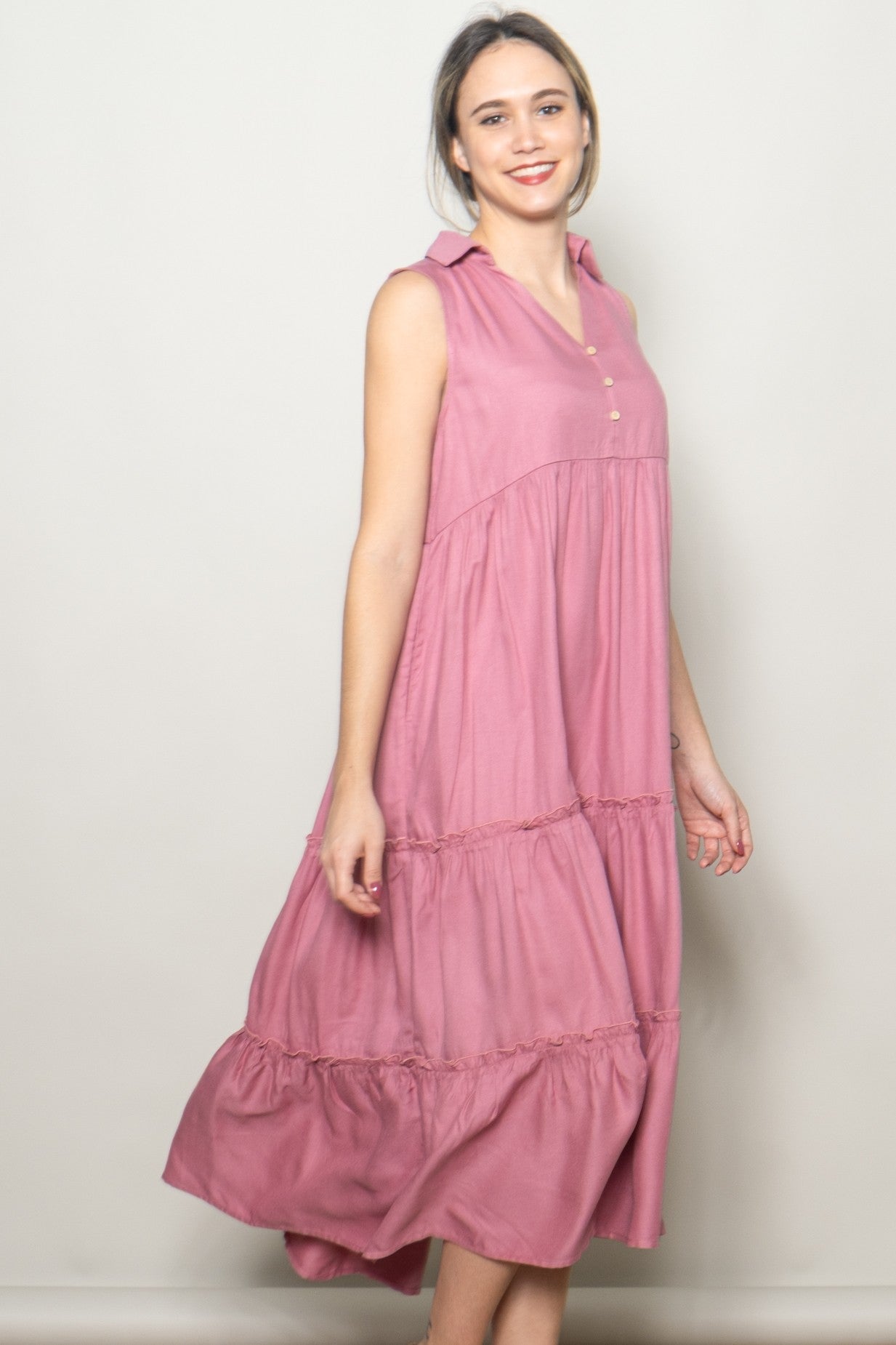 woman wearing a pink sleeveless tiered midi dress with buttons and a collared neckline