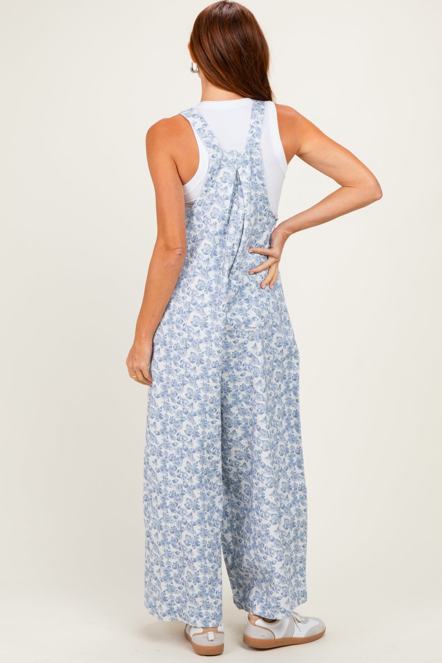woman wearing a backless blue and white floral jumpsuit with wide legs and a white tank top underneath