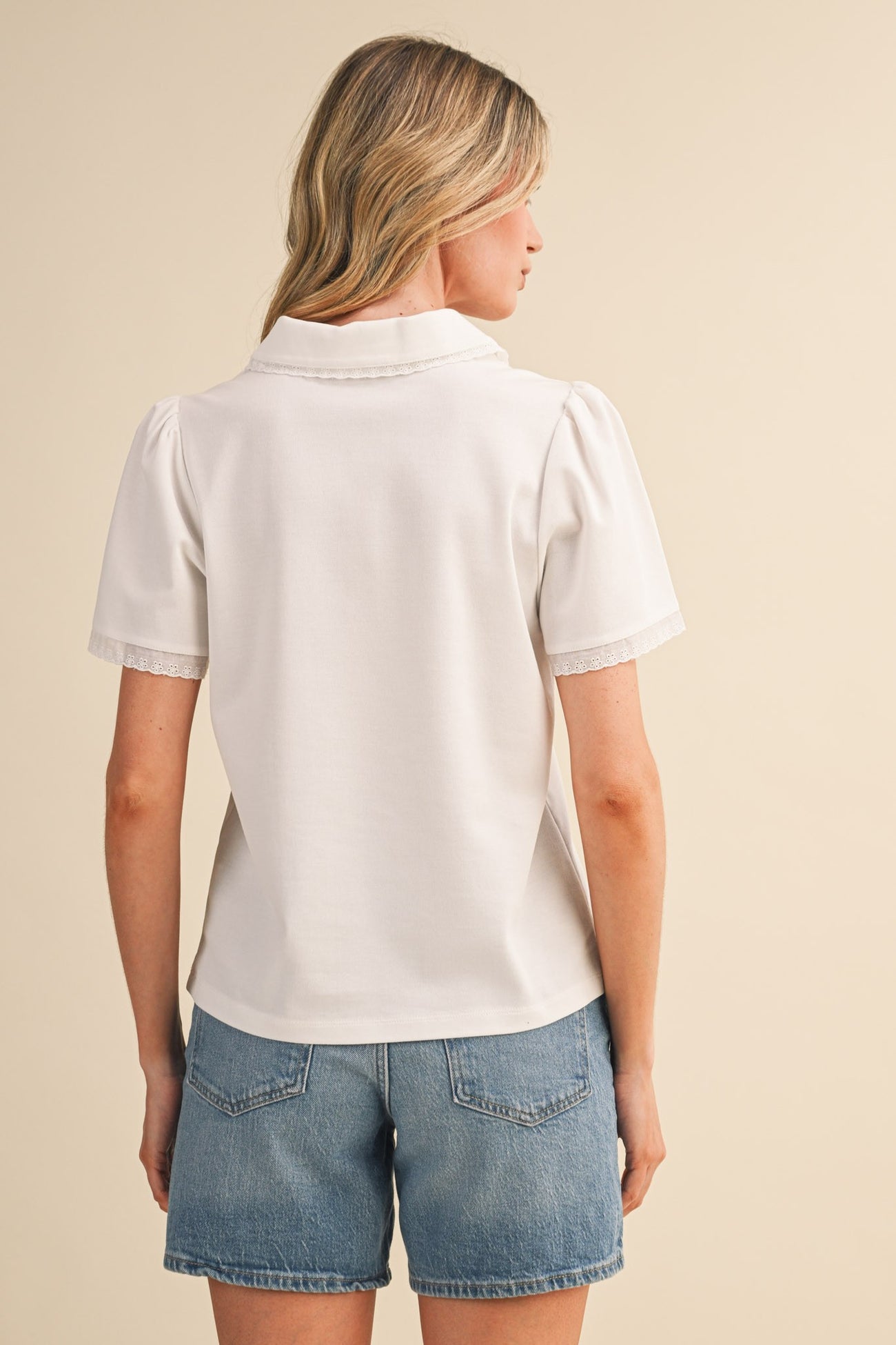 woman wearing a white short sleeve top with a collar and puff sleeves, paired with denim shorts