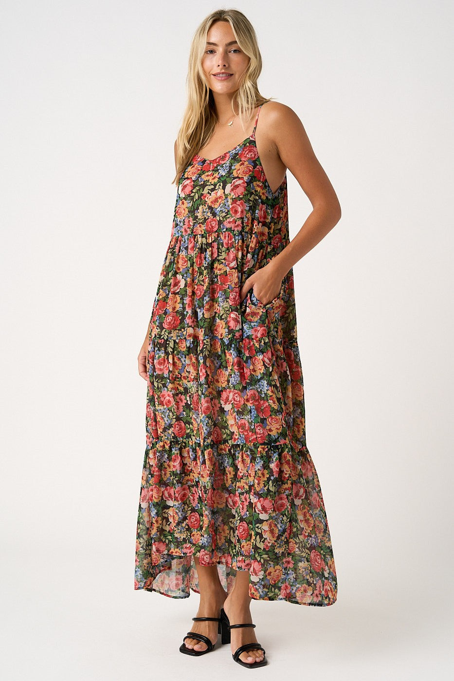 woman wearing a flowy maxi dress with a floral pattern and pockets, featuring adjustable spaghetti straps