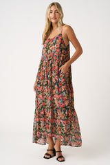 woman wearing a flowy maxi dress with a floral pattern and pockets, featuring adjustable spaghetti straps