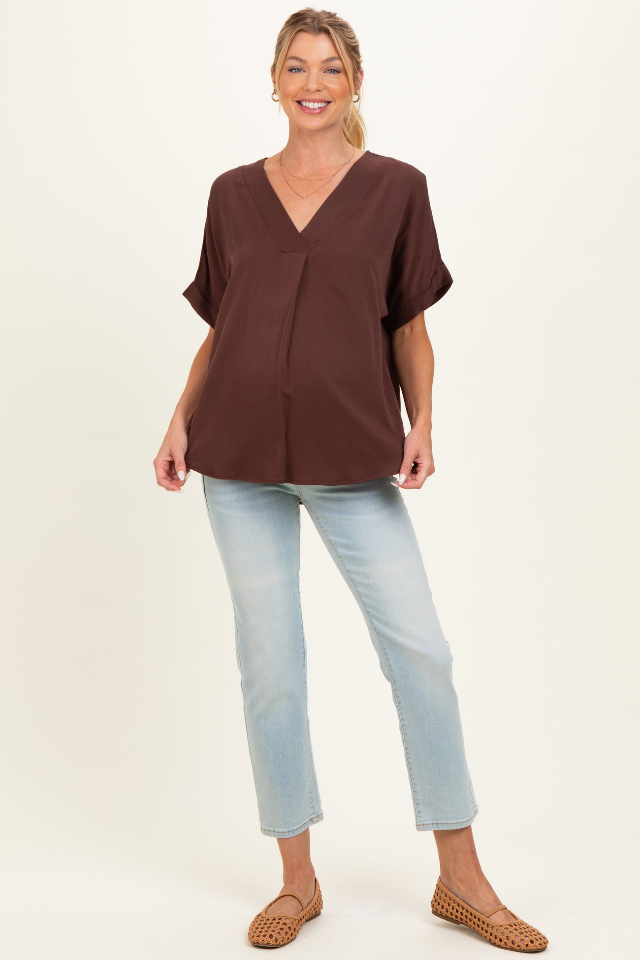 woman wearing a brown maternity top with a v-neckline and short sleeves, styled with light blue jeans