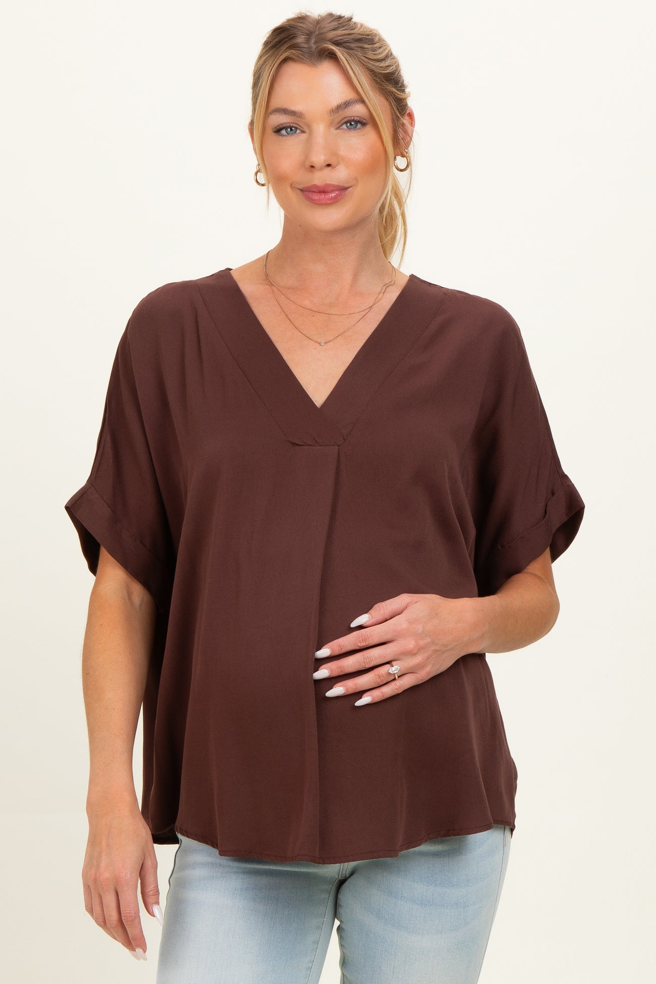 woman wearing a chocolate brown short sleeve maternity top and holding her baby bump