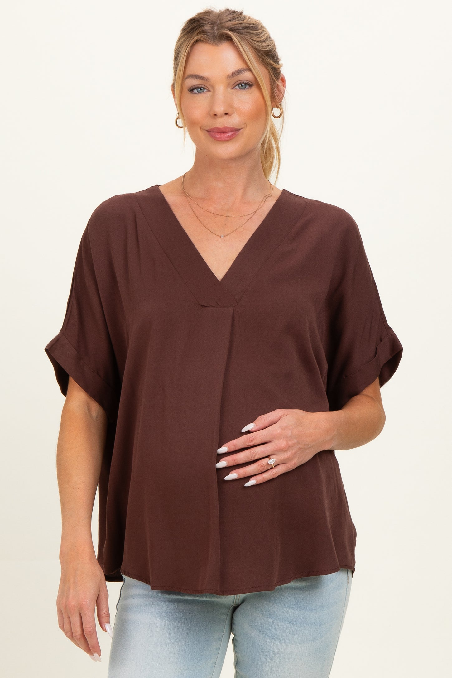 woman wearing a chocolate brown short sleeve maternity top and holding her baby bump