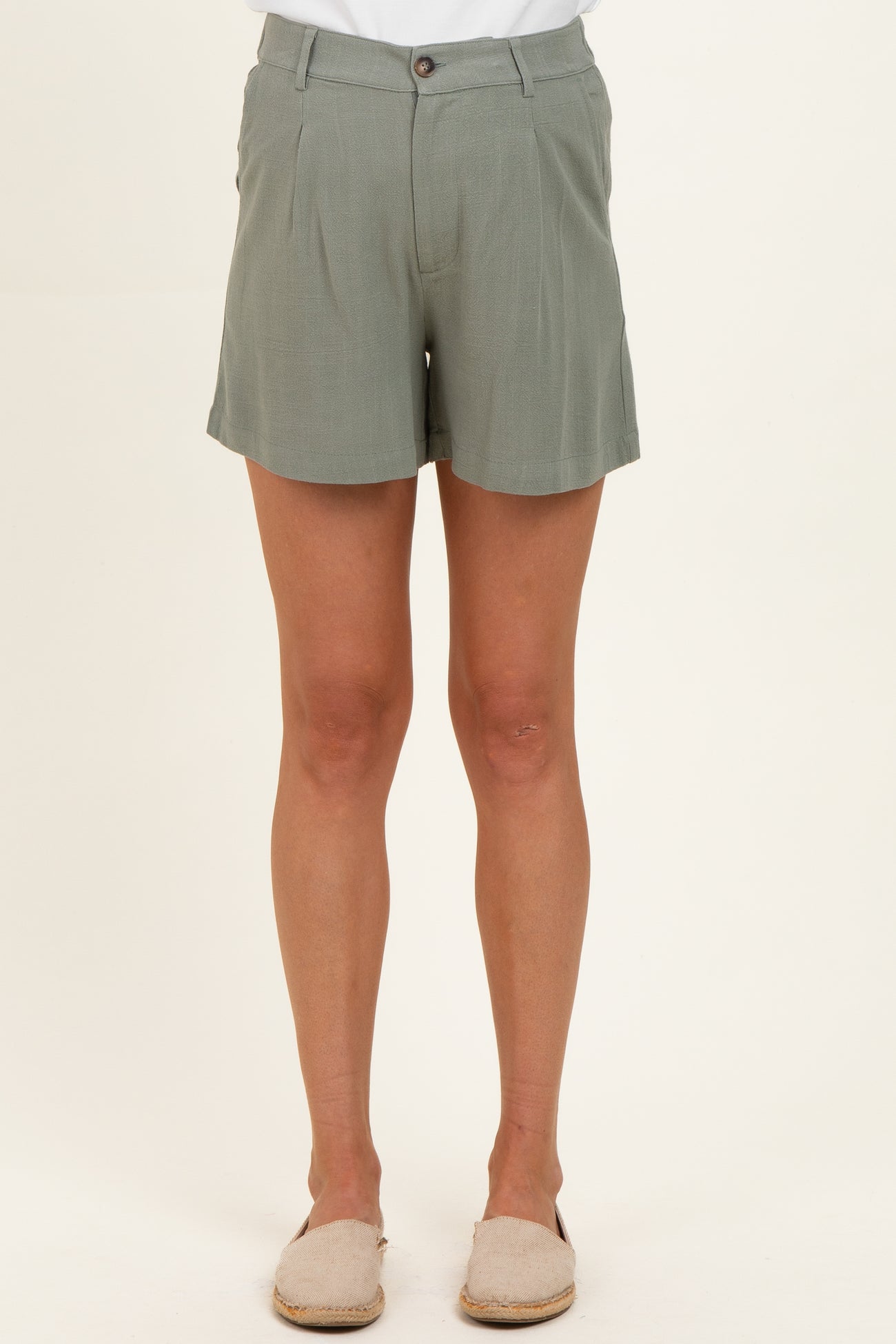 woman wearing light green maternity shorts with a button closure and pleat details