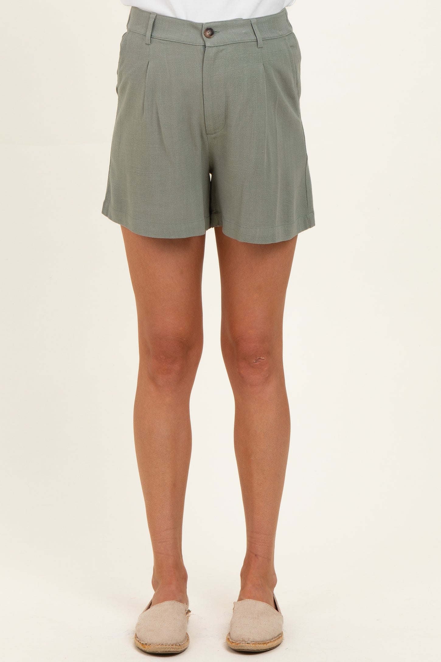 woman wearing light green maternity shorts with a button closure and pleat details