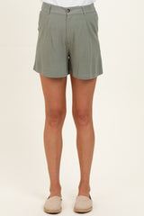 woman wearing light green maternity shorts with a button closure and pleat details