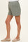 woman wearing light green maternity shorts with a relaxed fit and pleat details, paired with beige espadrilles