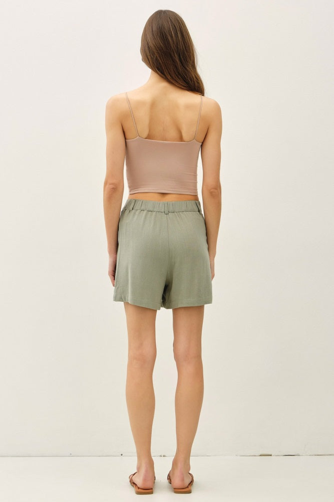 woman wearing a beige cropped tank top and olive green relaxed shorts, seen from the back