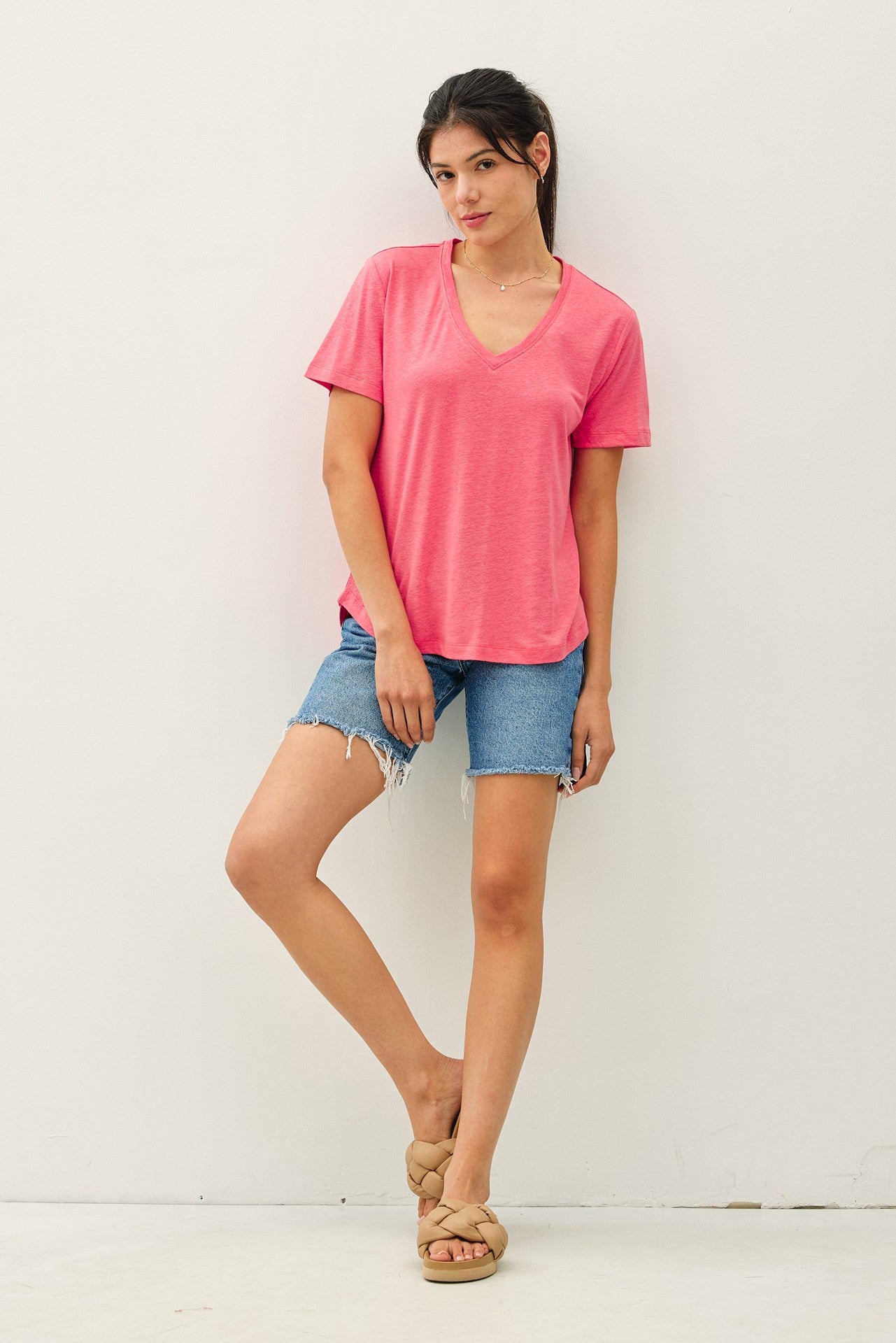 woman wearing a pink v-neck t-shirt and denim shorts, posing with one leg slightly forward