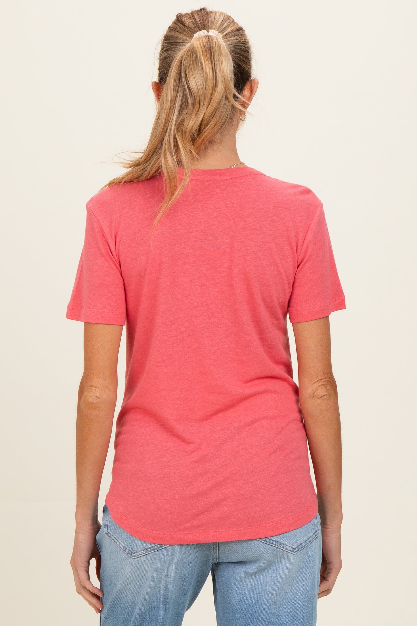 woman wearing a coral short sleeve maternity top, seen from the back with light blue jeans