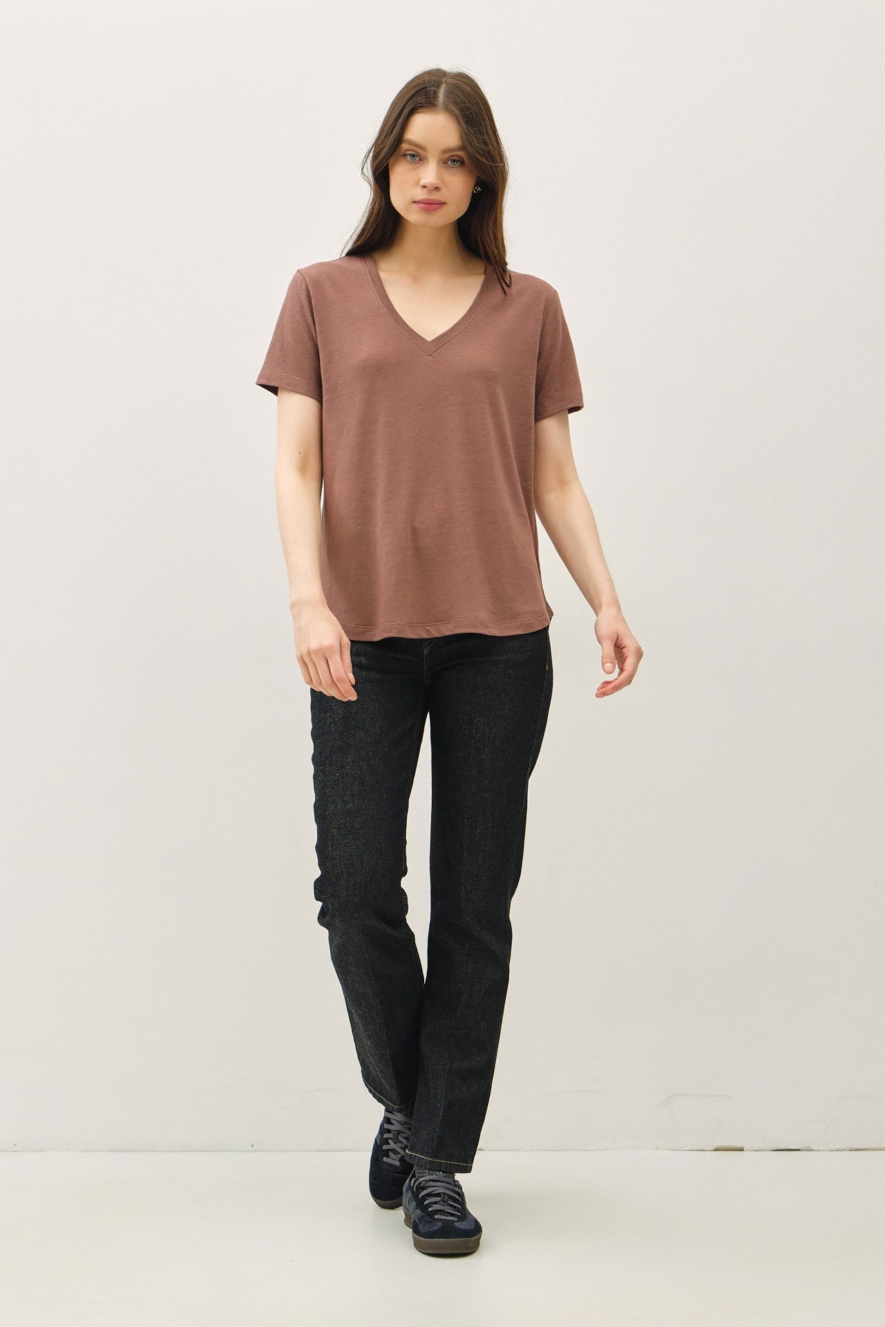 woman wearing a brown v-neck t-shirt and black jeans, walking confidently against a neutral background