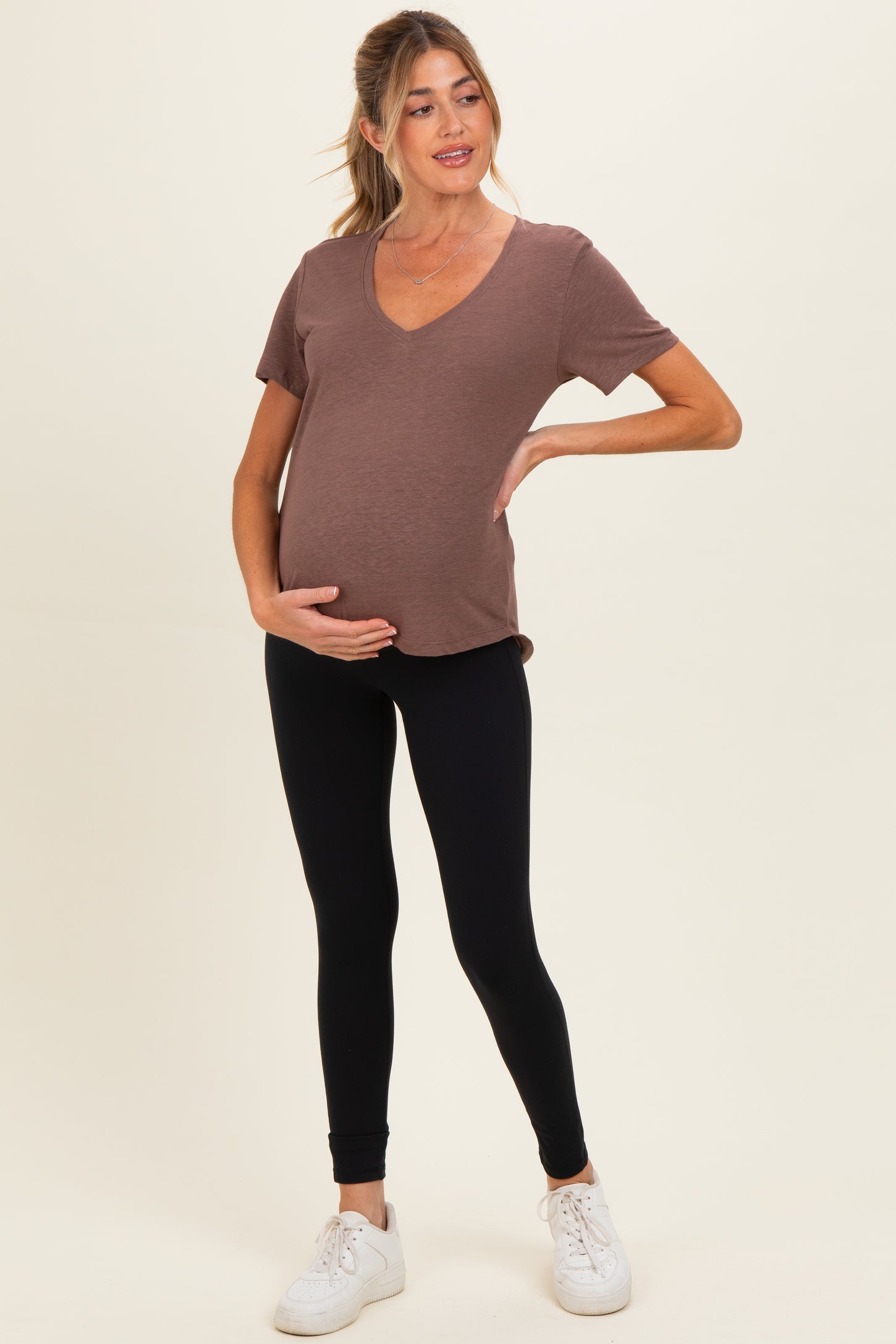 woman wearing a brown v-neck maternity top and black leggings, showcasing her baby bump