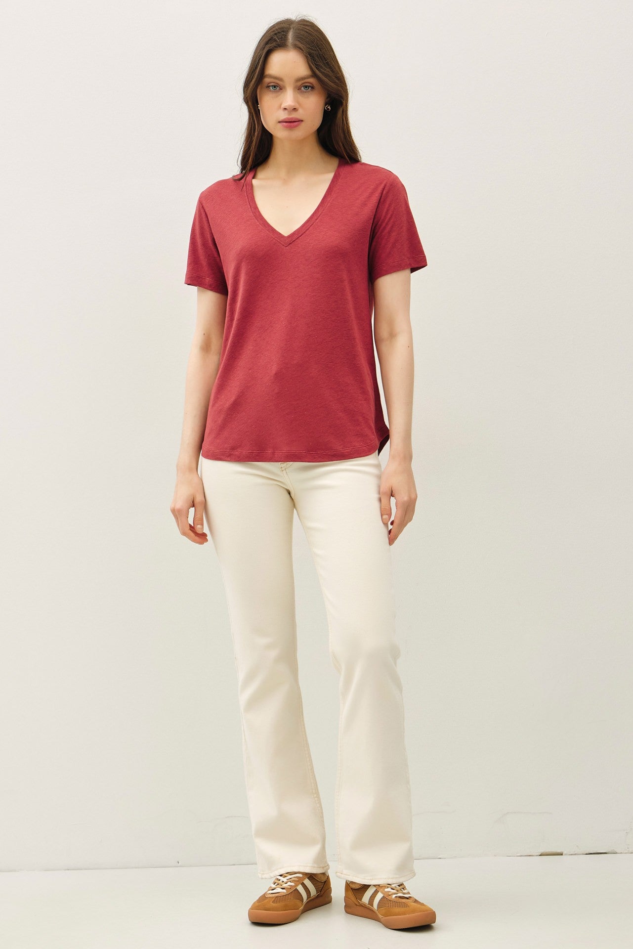 woman wearing a red v-neck t-shirt and white flared pants, standing with hands at her sides