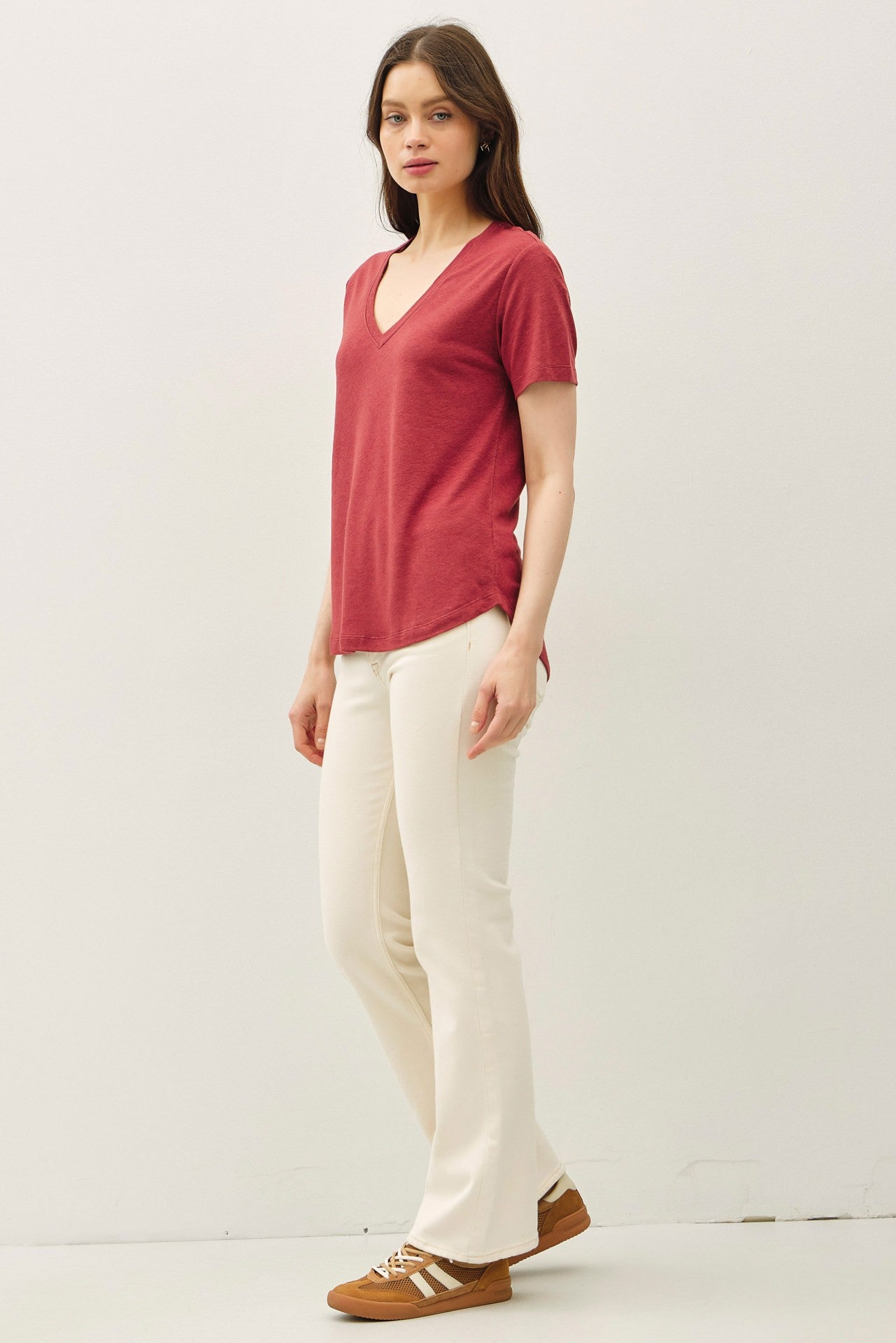 woman wearing a red v-neck t-shirt with short sleeves and cream flared pants, paired with brown sneakers