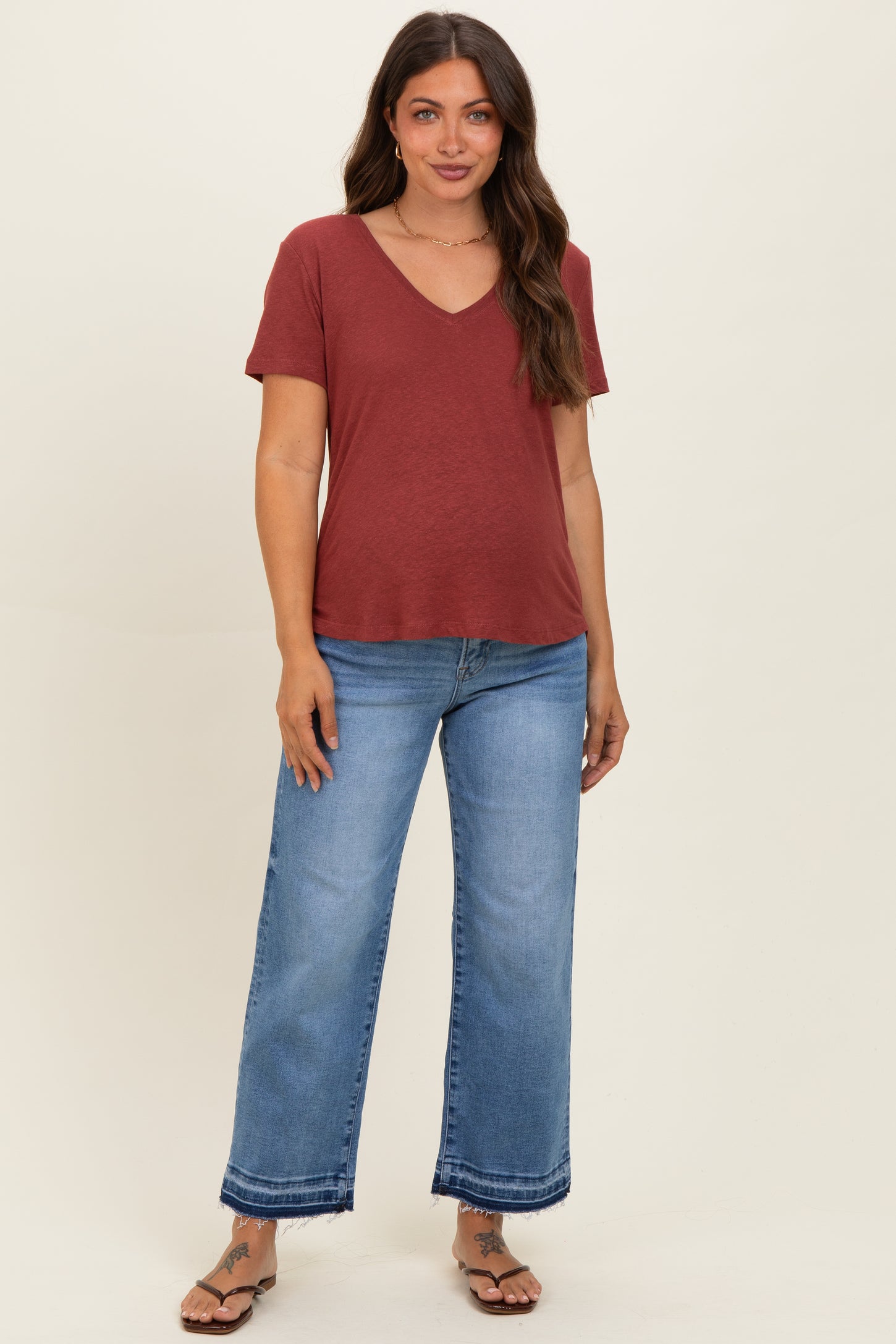 woman wearing a maroon v-neck maternity top with short sleeves and light blue wide-leg maternity jeans