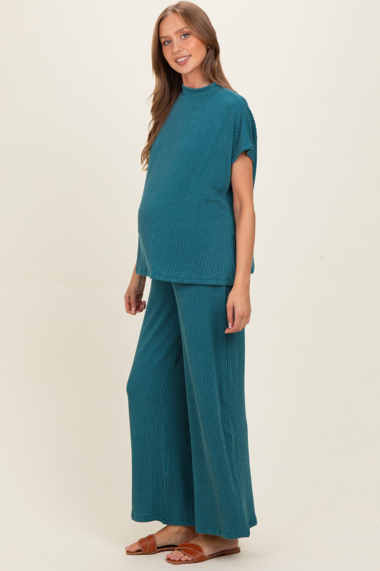 woman wearing a teal ribbed maternity top and wide-leg pants, visibly showing her baby bump