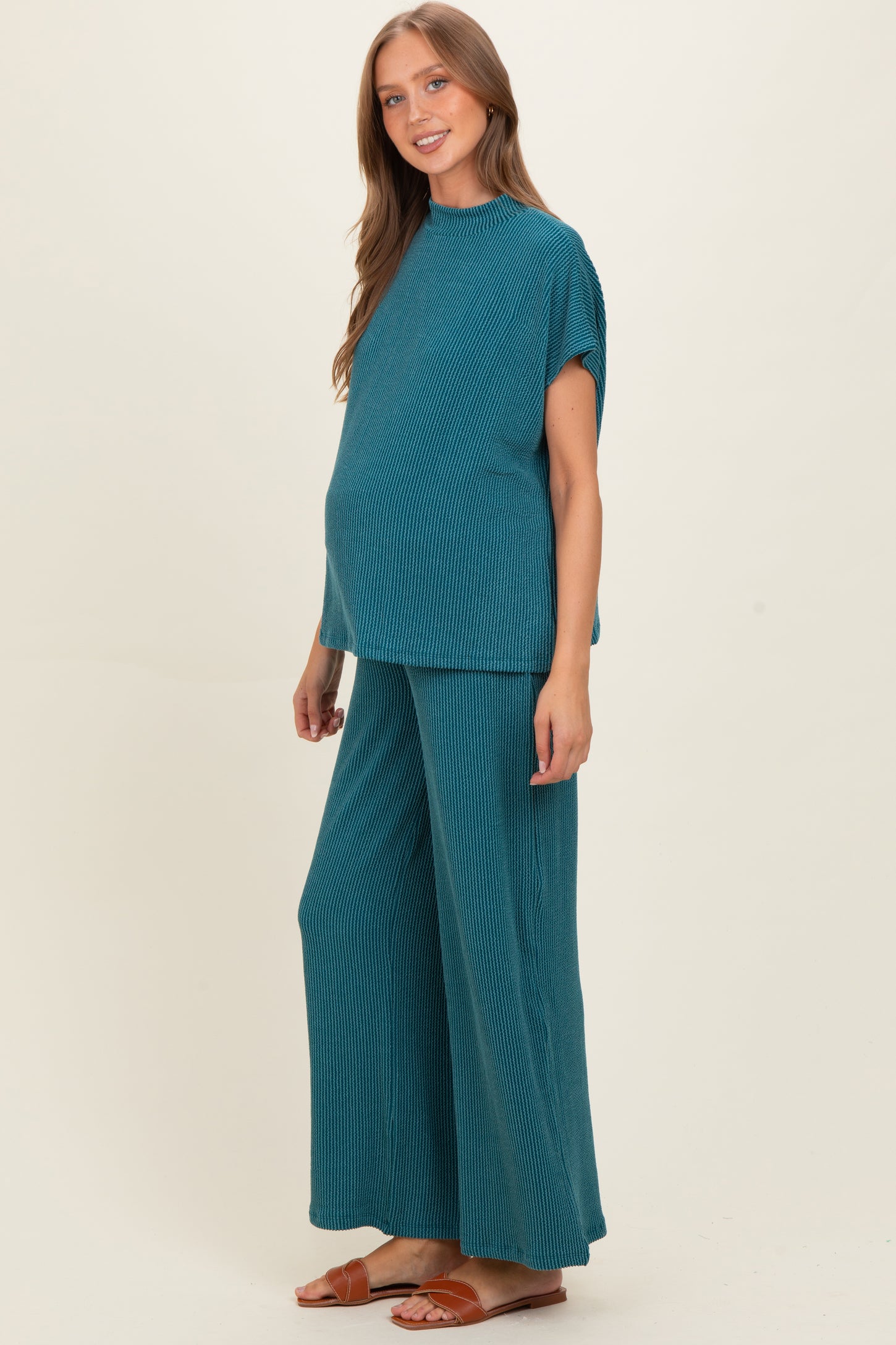 woman wearing a teal ribbed maternity top and wide-leg pants, visibly showing her baby bump