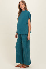 woman wearing a teal ribbed maternity top and wide-leg pants, visibly showing her baby bump