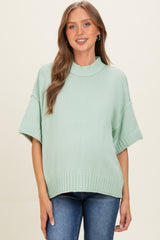 woman wearing a light green oversized maternity sweater with a mock neck and short sleeves