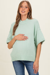 woman wearing a light green short sleeve maternity sweater and holding her baby bump