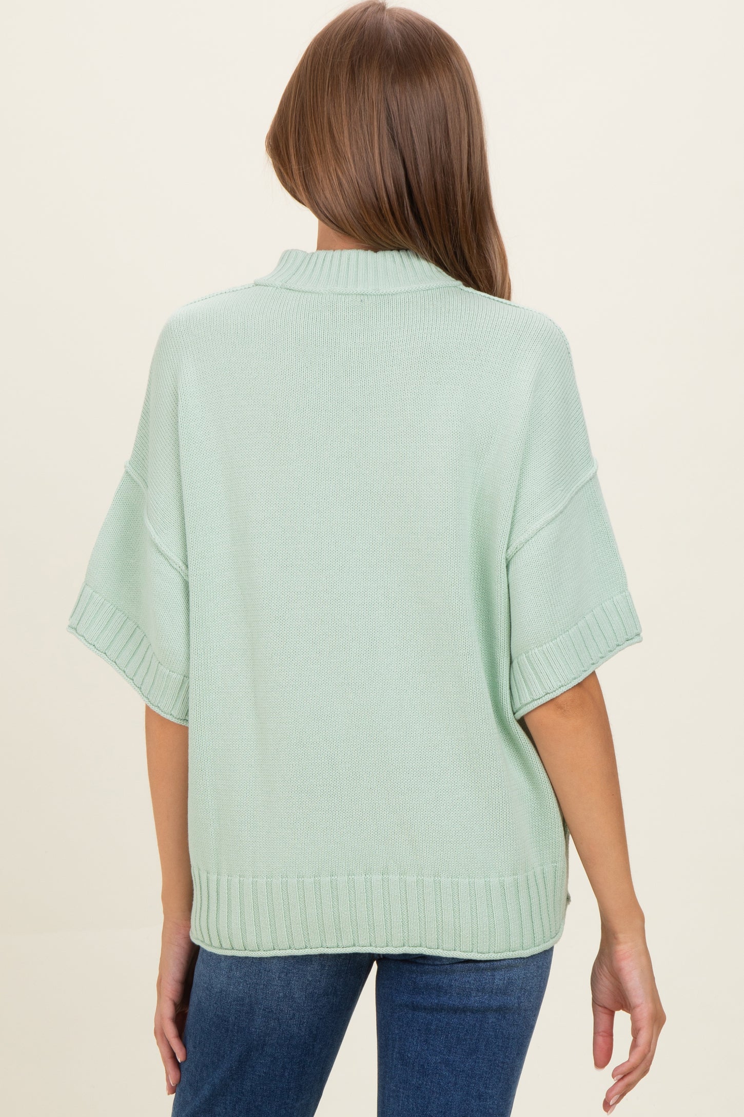 woman wearing a mint green oversized maternity sweater from the back, styled with jeans