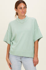 woman wearing a light mint green oversized knit sweater with a mock neck and short sleeves, paired with jeans