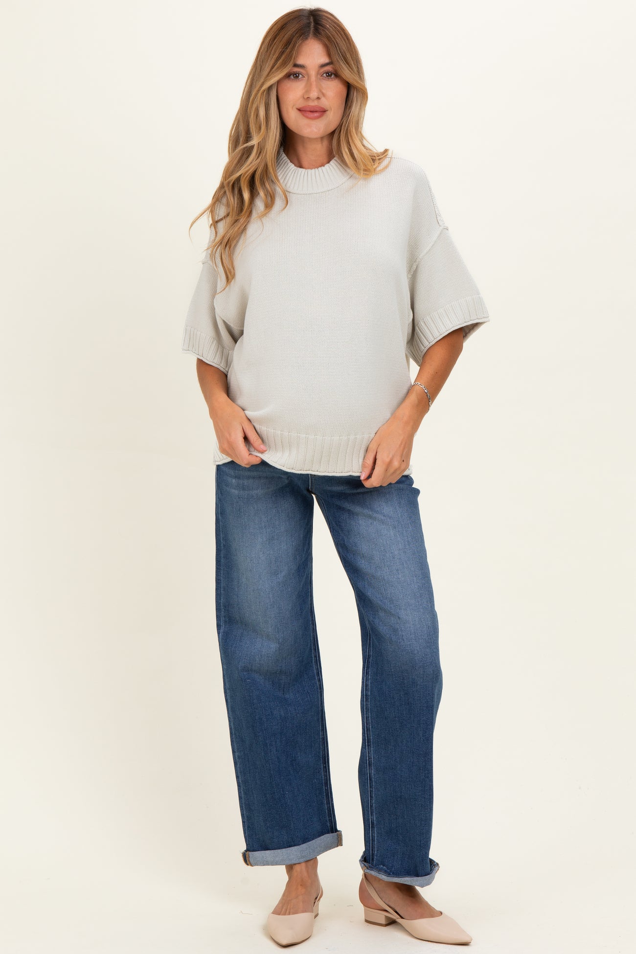 woman wearing a light gray oversized maternity sweater and blue wide-leg jeans