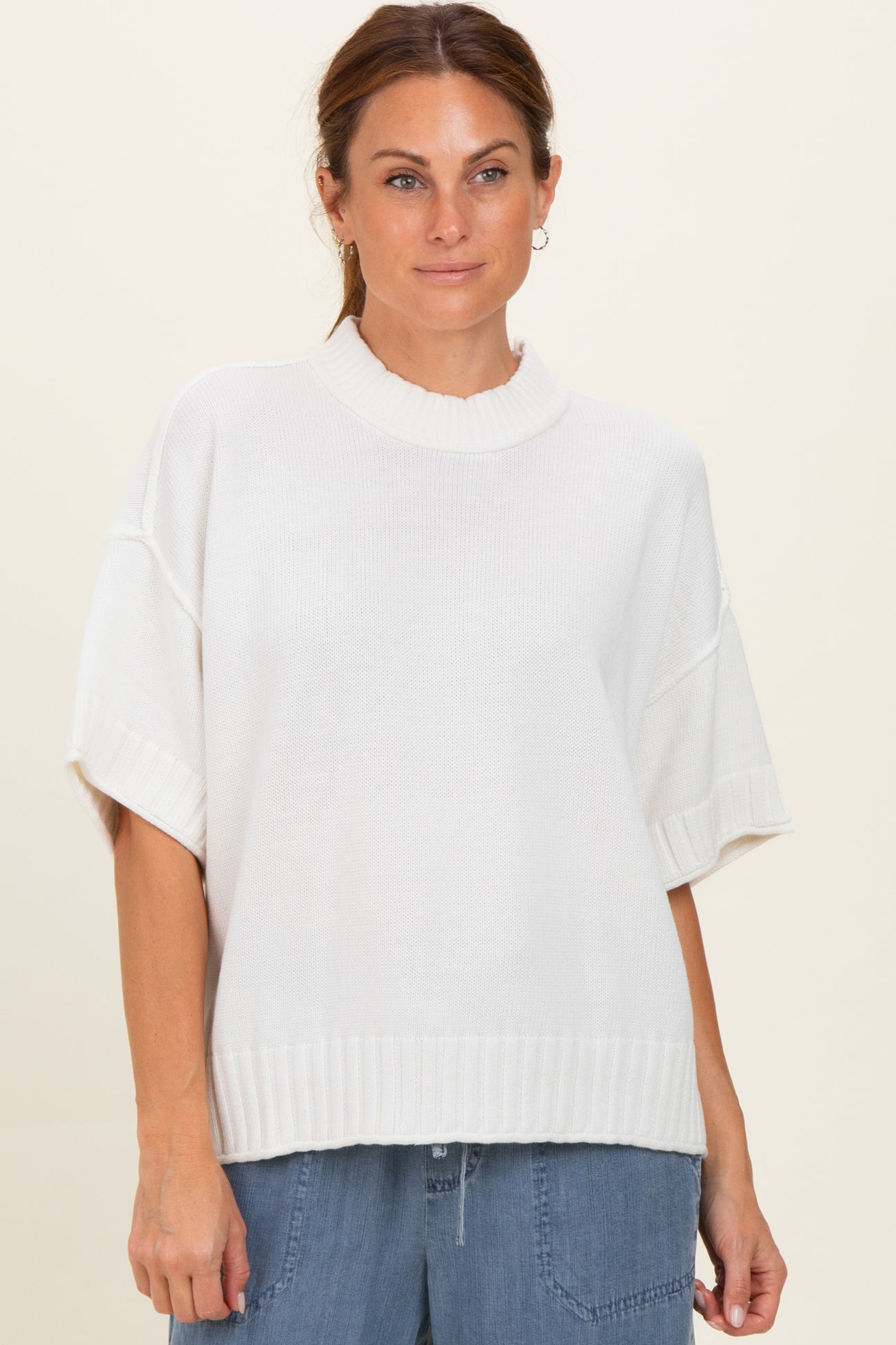 woman wearing a white oversized short sleeve sweater with a ribbed hem and mock neckline