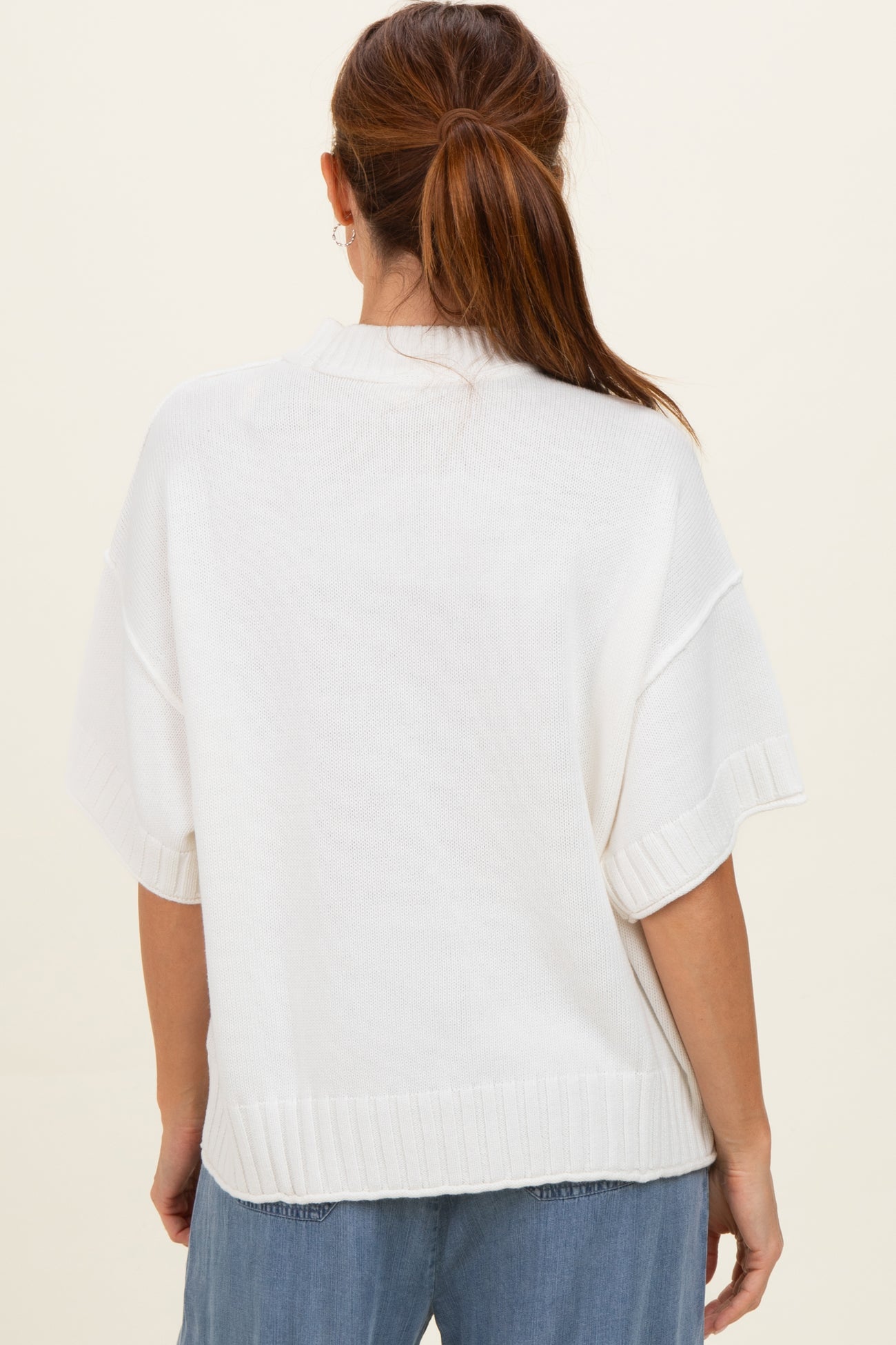 woman wearing a loose-fitting white knitted sweater with short sleeves and a ribbed hem, viewed from the back
