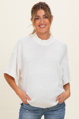 woman wearing a white oversized maternity sweater with short sleeves and a relaxed fit, cradling her baby bump