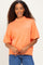 woman wearing an oversized coral knit sweater with a high neck and short sleeves, smiling at the camera