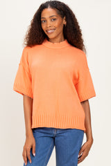 woman wearing an oversized orange knit sweater with short sleeves and a ribbed hem, paired with blue jeans