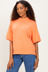 woman wearing an oversized bright orange short sleeve sweater with a ribbed hem and standing in front of a neutral background
