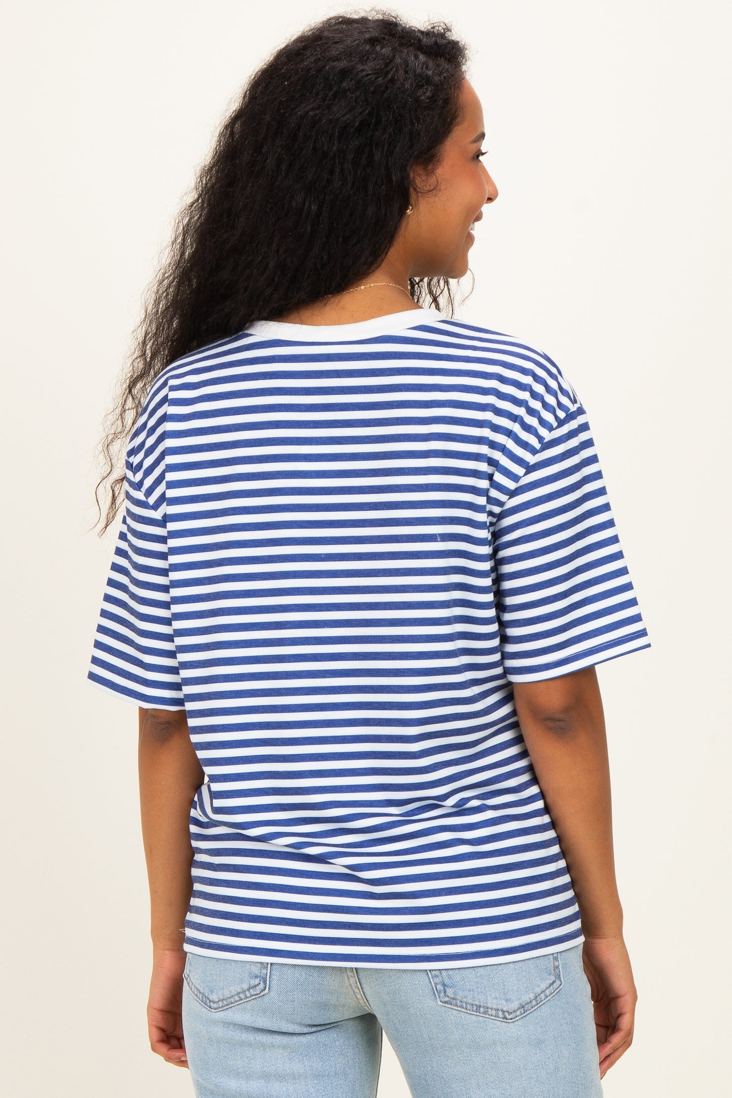 woman wearing a blue and white striped maternity top, facing away, with curly hair and casual denim jeans