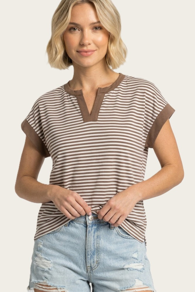 woman wearing a brown and cream striped short sleeve top with a v-neckline and rolled cuffs, styled with distressed denim shorts