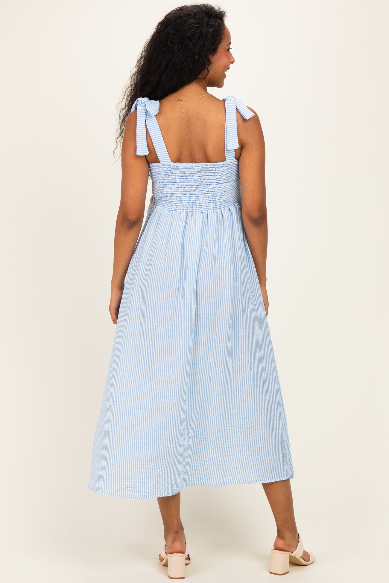 woman wearing a light blue and white striped maternity dress with tie straps and a smocked back