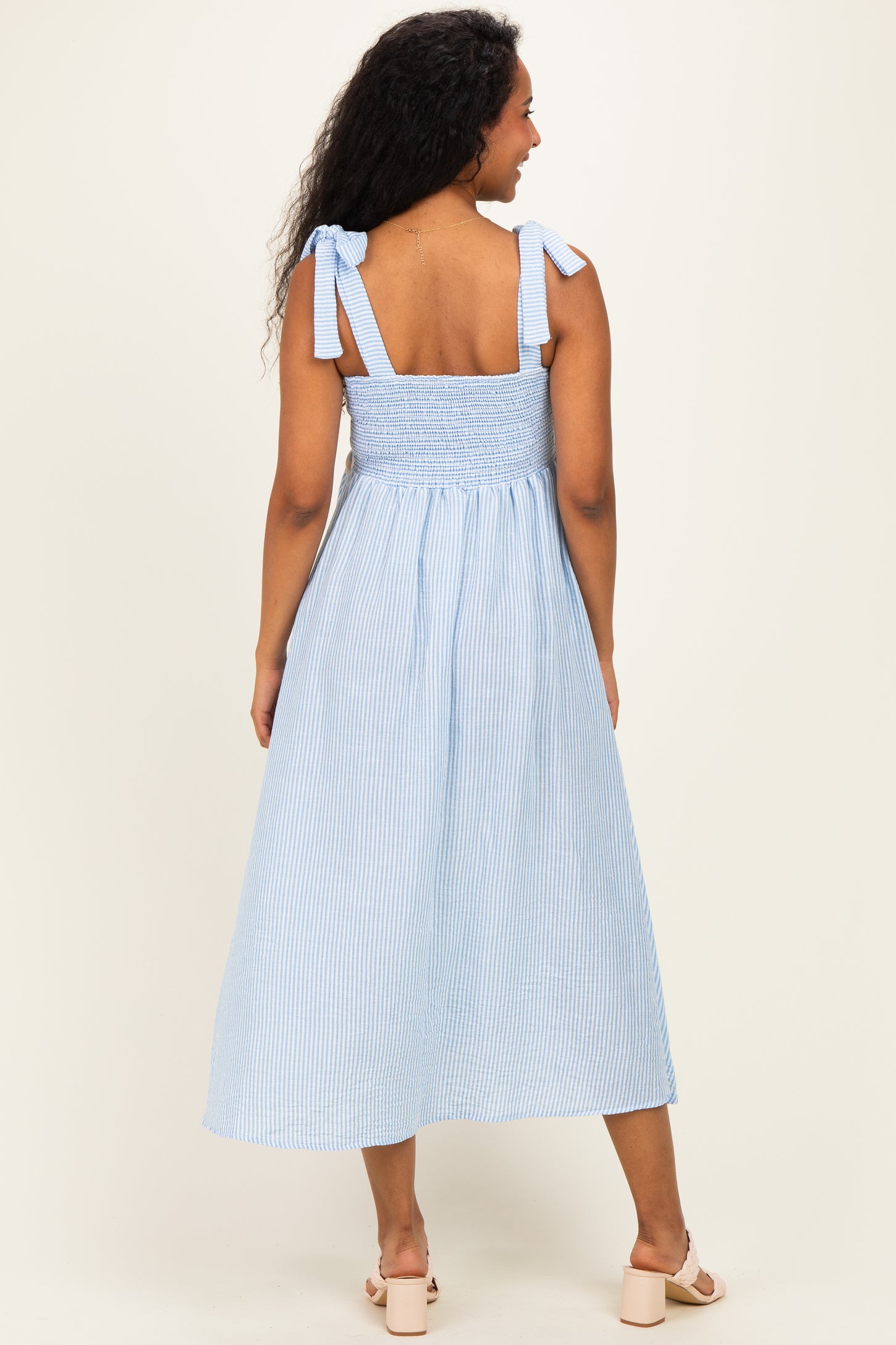 woman wearing a light blue and white striped maternity dress with tie straps and a smocked back