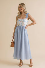 woman wearing a floral and striped maxi dress with tie straps and a fitted bodice, holding a small brown handbag