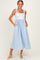 woman wearing a light blue striped sundress with floral bodice and pockets, standing on a neutral background