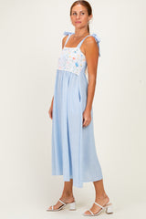 woman wearing a blue and white striped midi dress with floral embroidery and adjustable shoulder ties