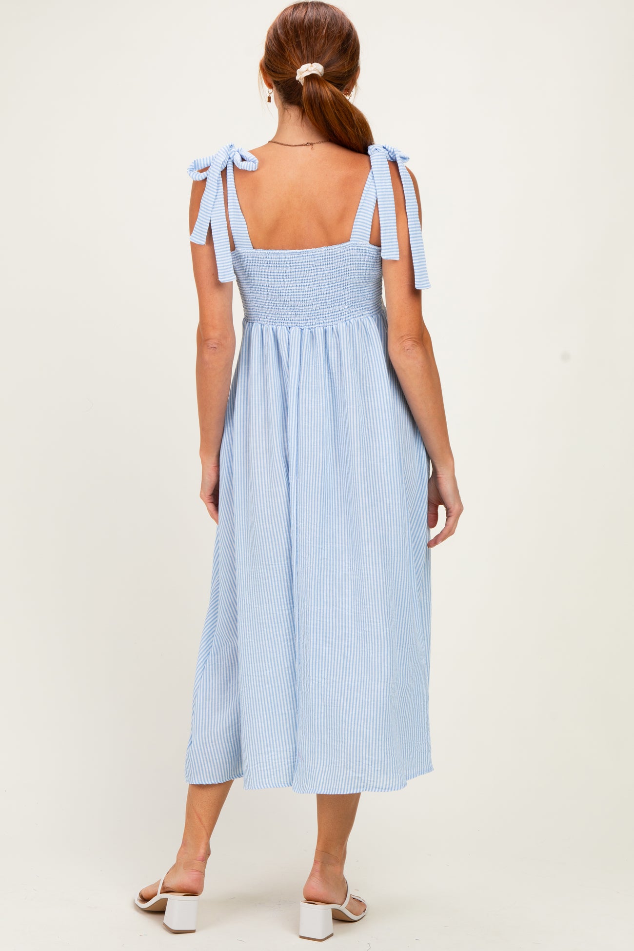 woman wearing a blue and white striped sleeveless dress with tie straps and a smocked back, seen from the back