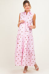 woman wearing a pink polka dot maxi maternity dress with a belted waist and sleeveless design, showing off her baby bump