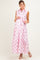 woman wearing a pink polka dot maxi maternity dress with a belted waist and sleeveless design, showing off her baby bump