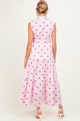 woman wearing a pink sleeveless maternity dress with brown polka dots and a tiered skirt, showing a baby bump from the back
